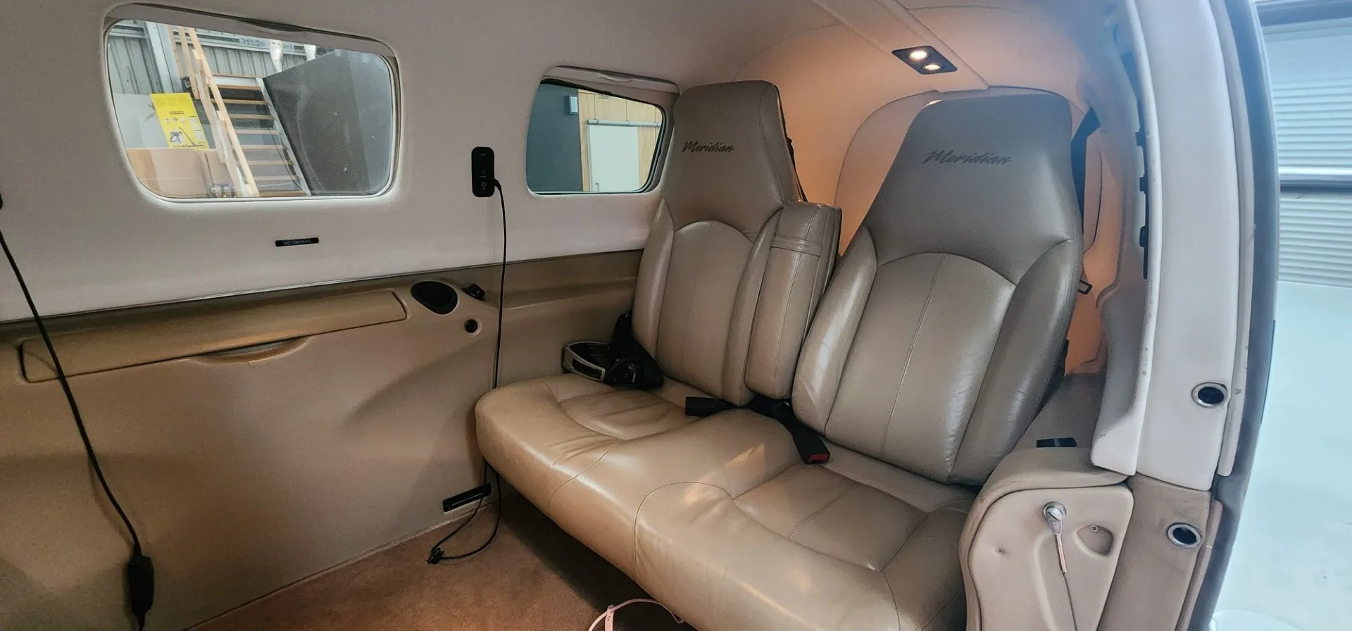 The tan leather passenger seats of an aircraft cabin, with "Meridian" embroidered on the headrests.
