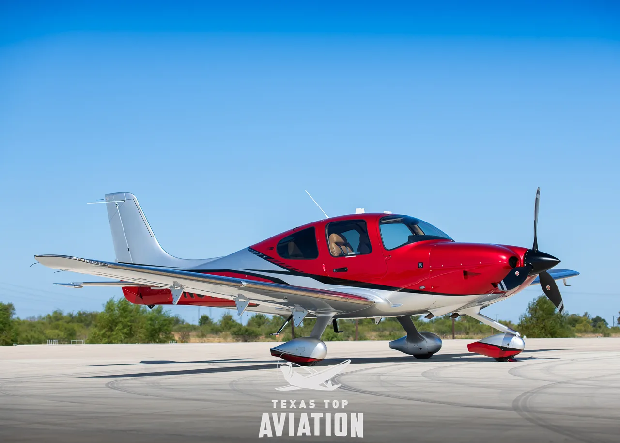 A red and silver Cirrus SR22T GTS aircraft parked on an tarmac with trees in the background.