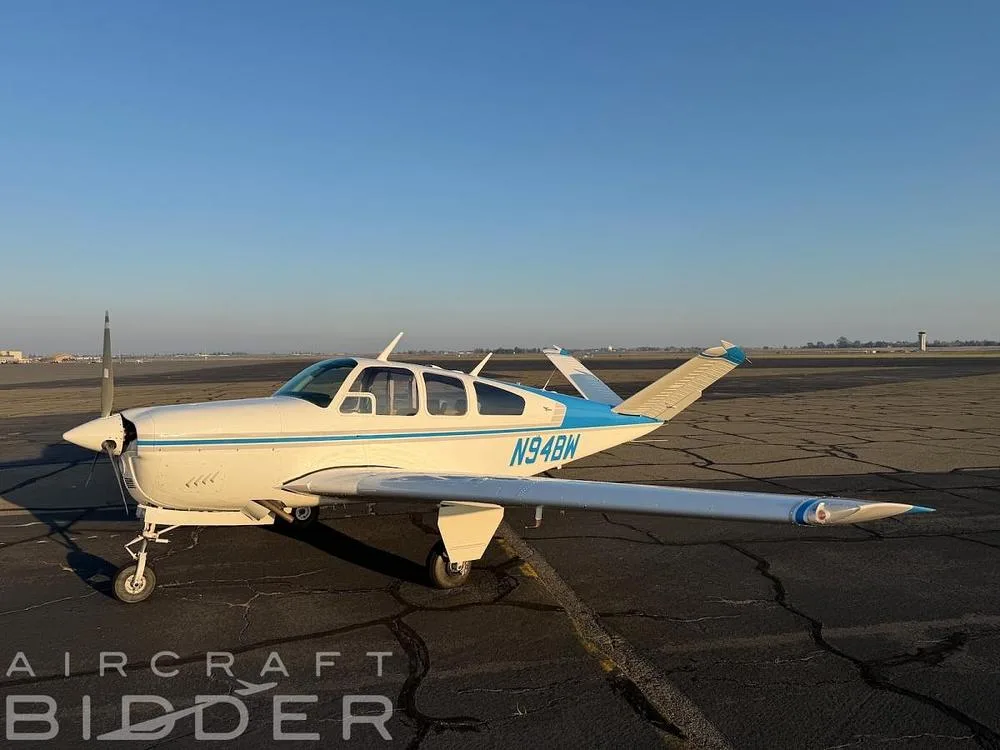 A white Beechcraft Bonanza with blue stripes, registration N94BW, parked on an airfield under a clear sky.