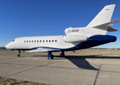 A white and blue Dassault Falcon 900EX, registration C-GEOS, parked on the tarmac.