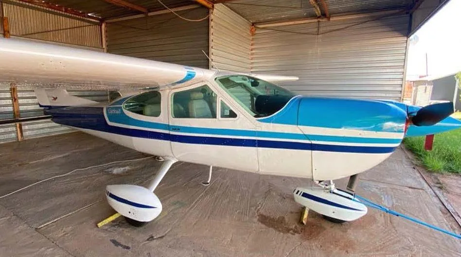 A white and blue Cessna 210 Centurion aircraft parked inside a hangar.