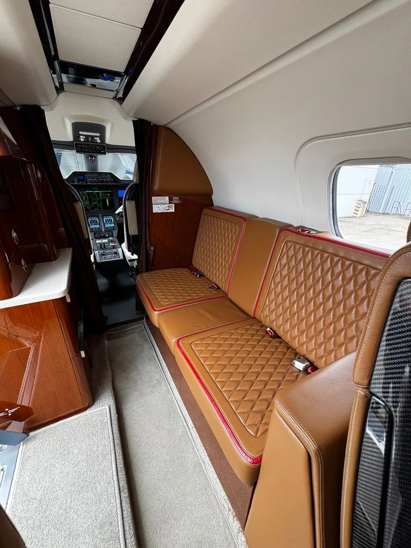 A side view of the aircraft cabin showing a brown quilted leather bench seat and a glimpse of the cockpit.