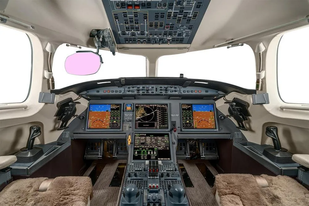 The cockpit of a Dassault Falcon 900EX, showing the instrument panel with multiple display screens and overhead controls.