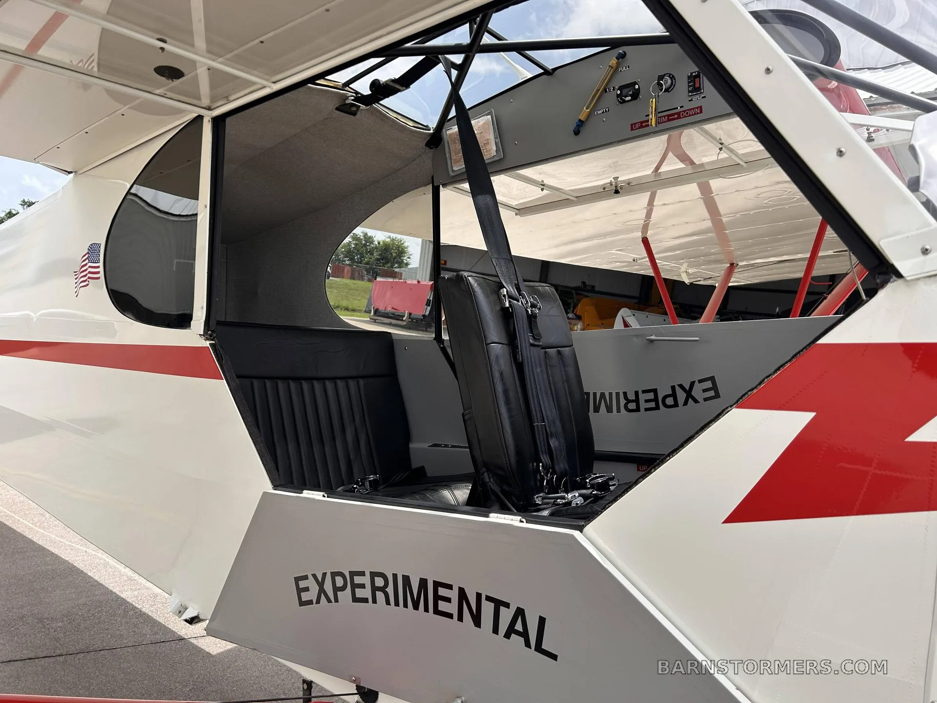 The open cabin door of the white and red aircraft, revealing black seats and the "EXPERIMENTAL" marking on the fuselage.