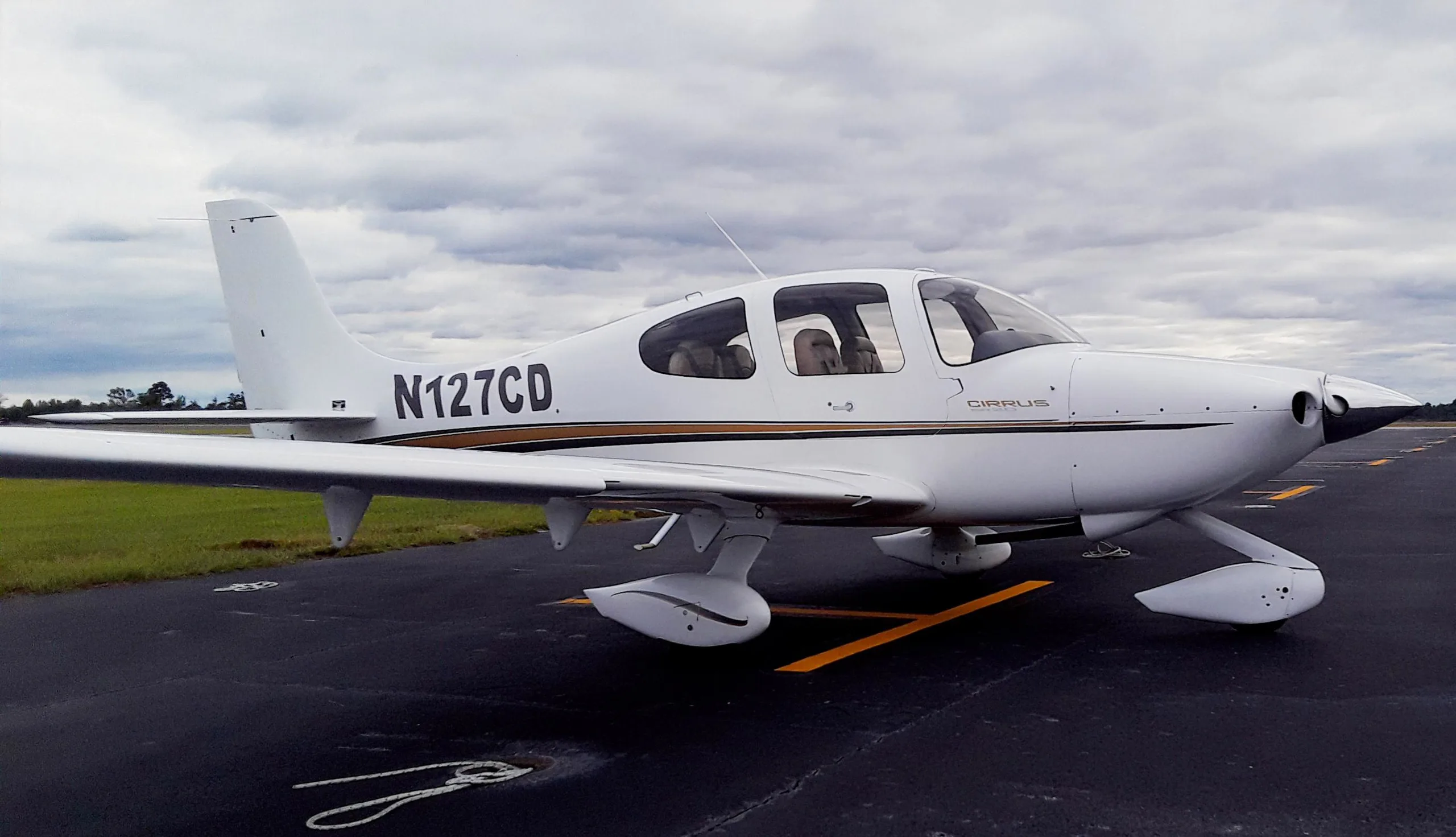A white Cirrus aircraft with registration N127CD is parked on an asphalt tarmac under a cloudy sky.