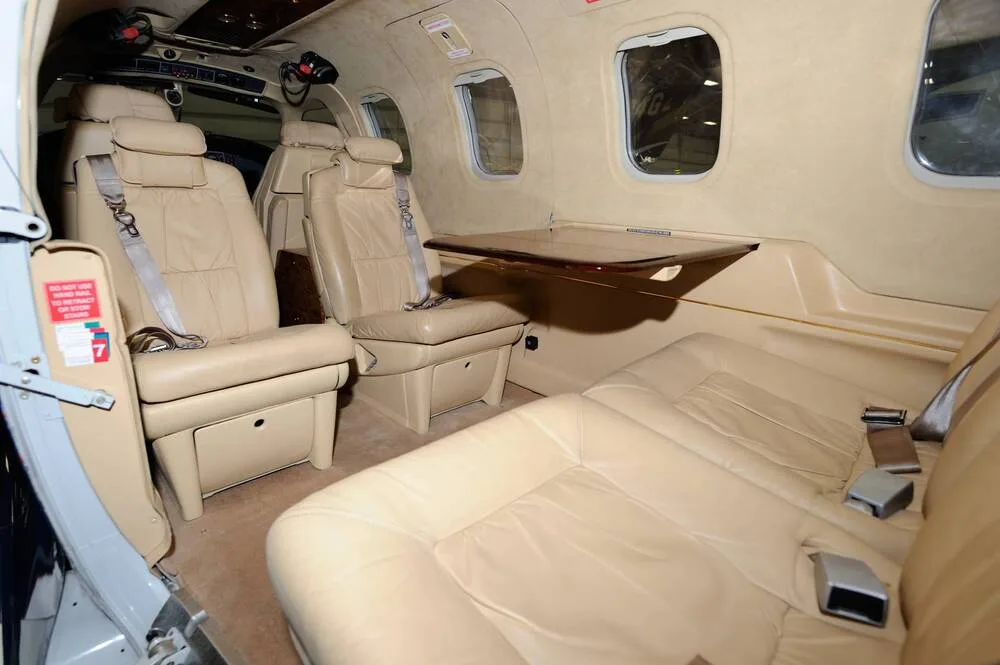 The interior cabin of the TBM 850 aircraft, featuring beige leather seats and a small wooden table.