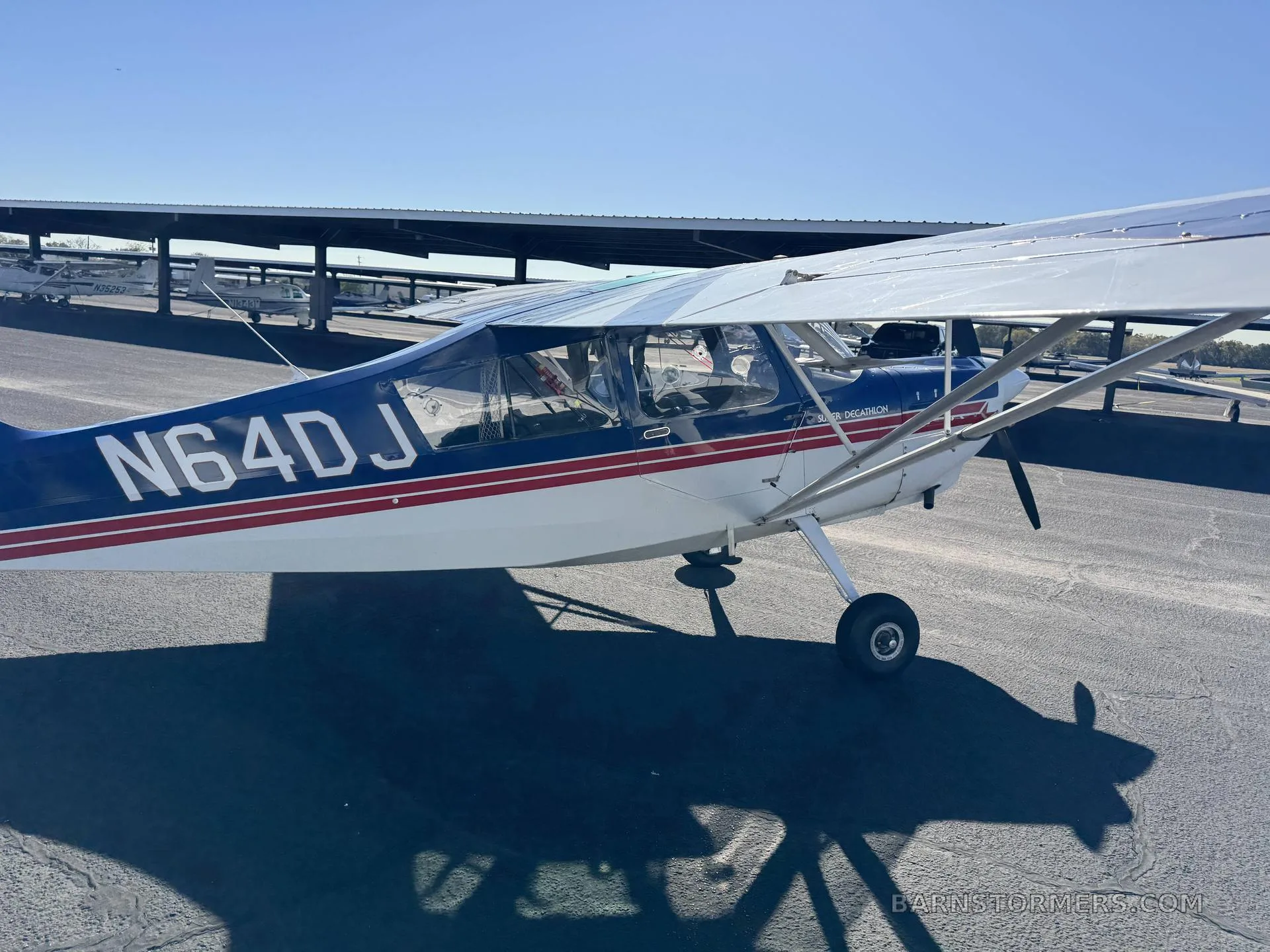 A blue and white Super Decathlon aircraft with red stripes and registration N64DJ parked on an airfield.