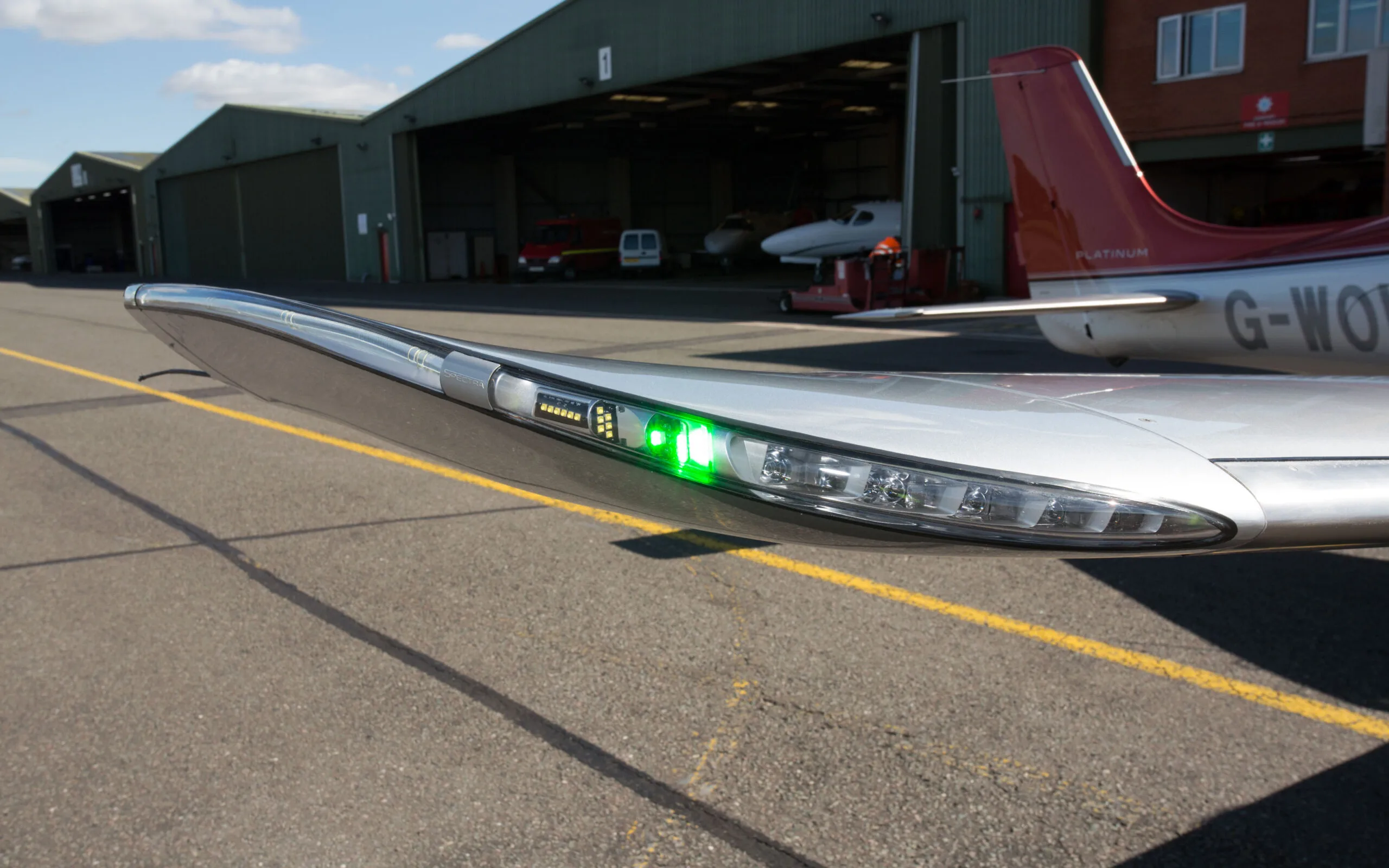 A close-up of the right wingtip of a Cirrus SR22T GTS aircraft, showing the green navigation light illuminated on an airfield.