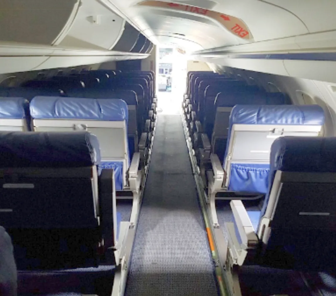 The interior cabin of an aircraft features rows of blue economy seats and an aisle leading to the rear.