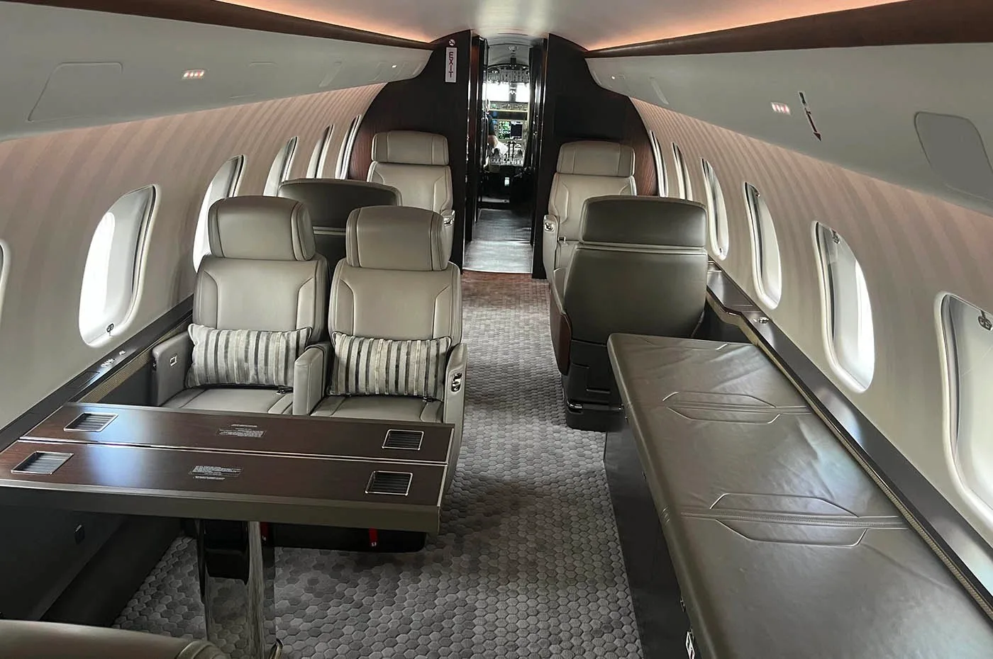 A view of the business jet cabin showing grey leather seats, a dining table, and a side divan.