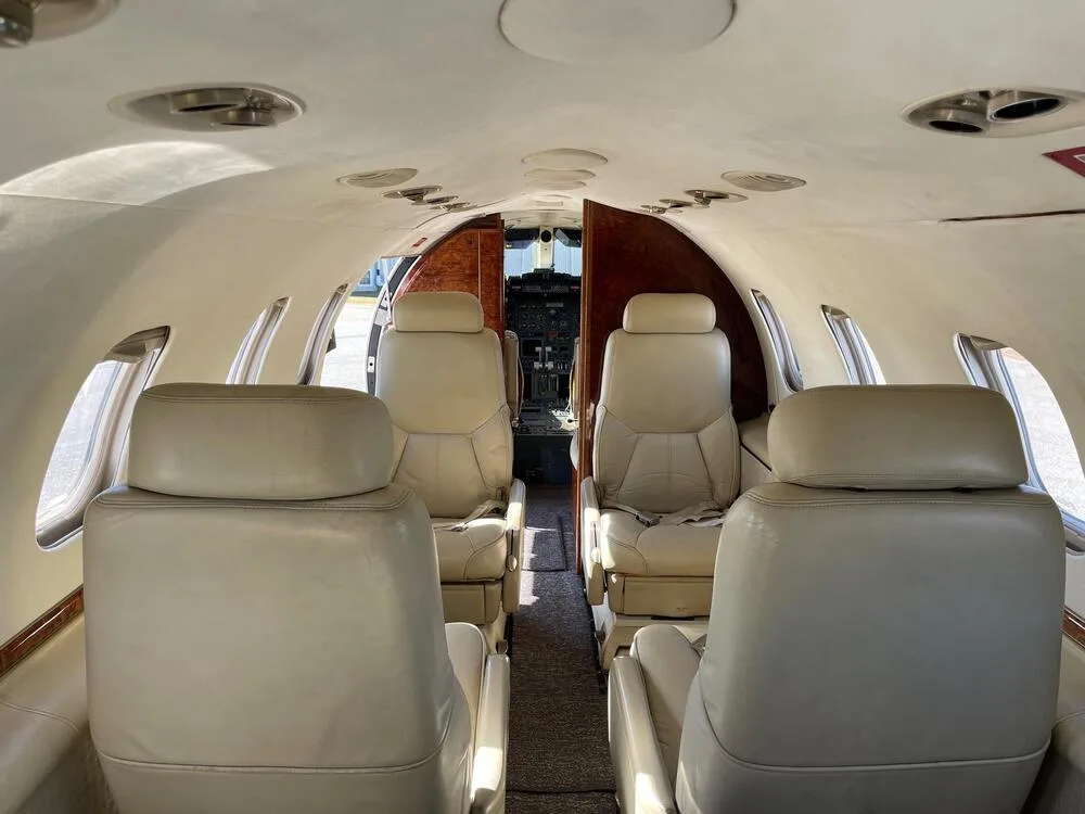 View from the rear of the aircraft cabin, showing beige leather seats and the cockpit entrance.