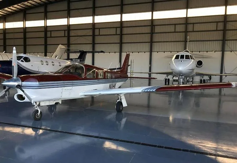A burgundy and white single-engine aircraft, N11HK, parked in a hangar with other planes.