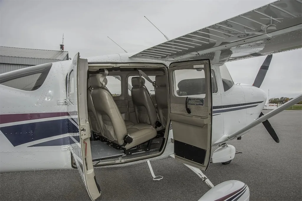The open doors of a white single-engine propeller aircraft reveal its tan leather cabin seats.