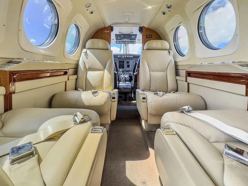 A wide-angle view of a luxurious beige leather aircraft cabin interior, with sunlight streaming through the windows.