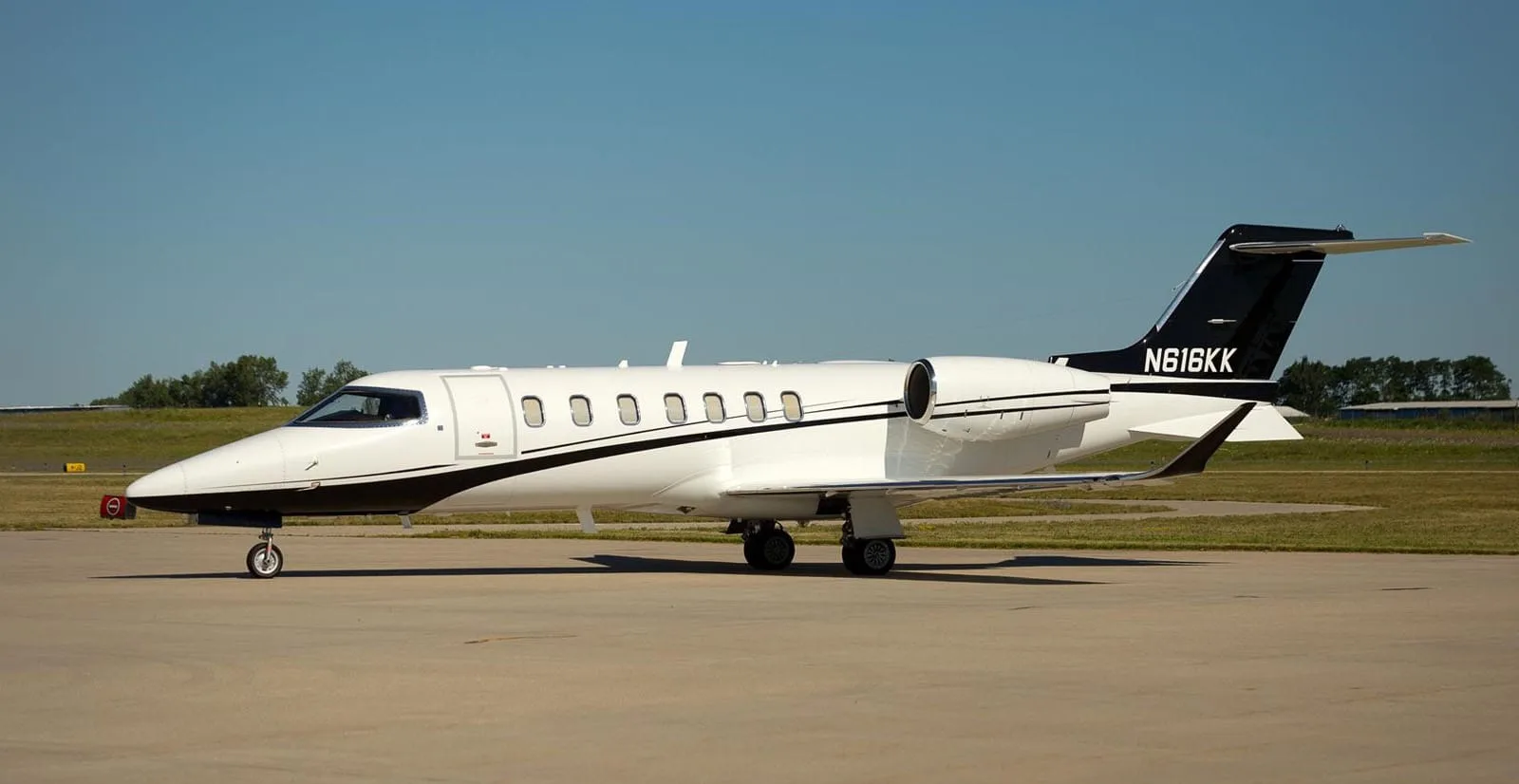A white business jet with black stripes and tail, registration N618BKK, parked on an airfield under a clear sky.