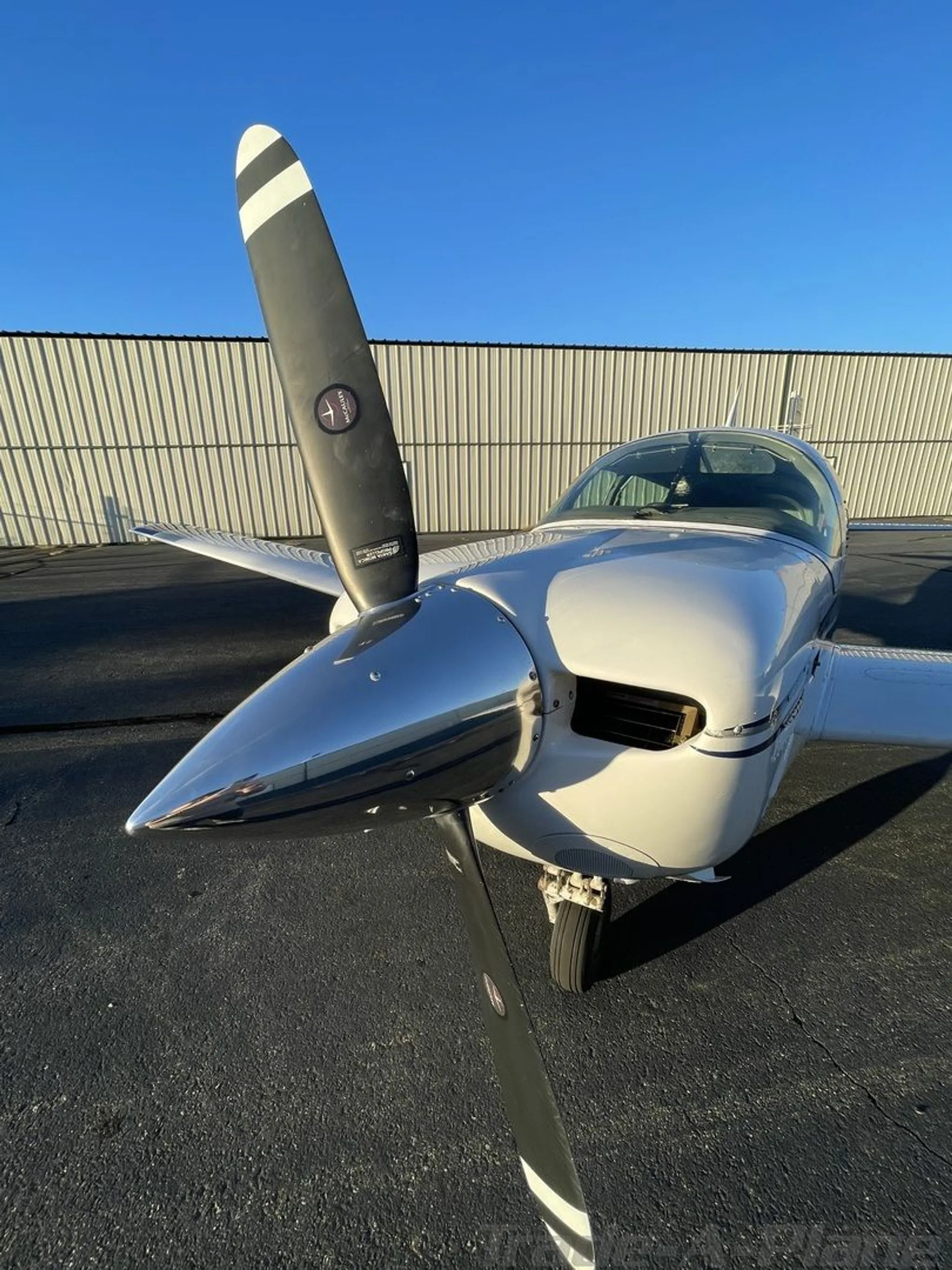A close-up front view of the propeller and polished spinner of the white aircraft on an airfield.