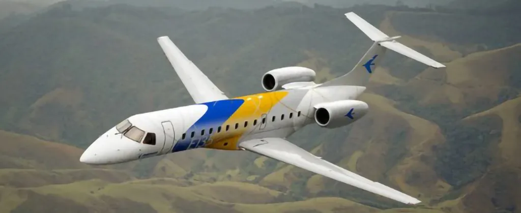 A white, blue, and yellow Embraer ERJ-145 aircraft flies over green, rolling hills.