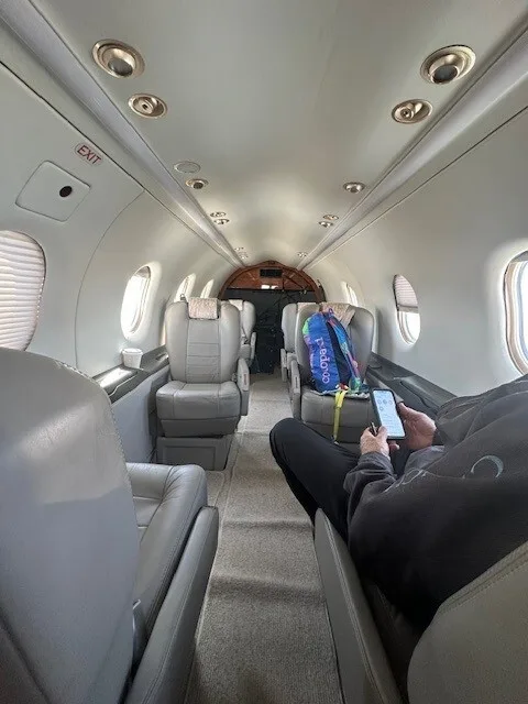 The interior cabin of an aircraft with grey seats and a person sitting on the right, looking towards the cockpit.
