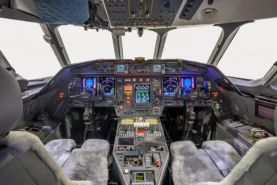 The illuminated cockpit of a private jet with multiple digital displays and controls.