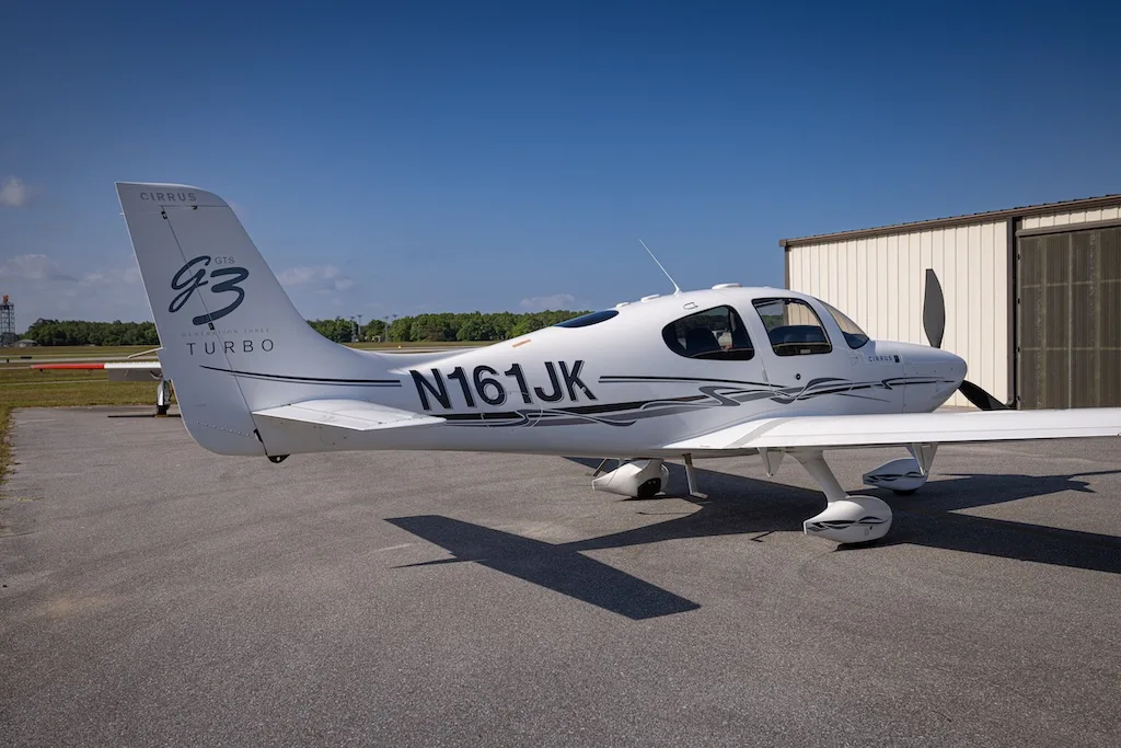A white Cirrus SR22 G3 Turbo aircraft, registration N161JK, parked on an asphalt tarmac next to a hangar.