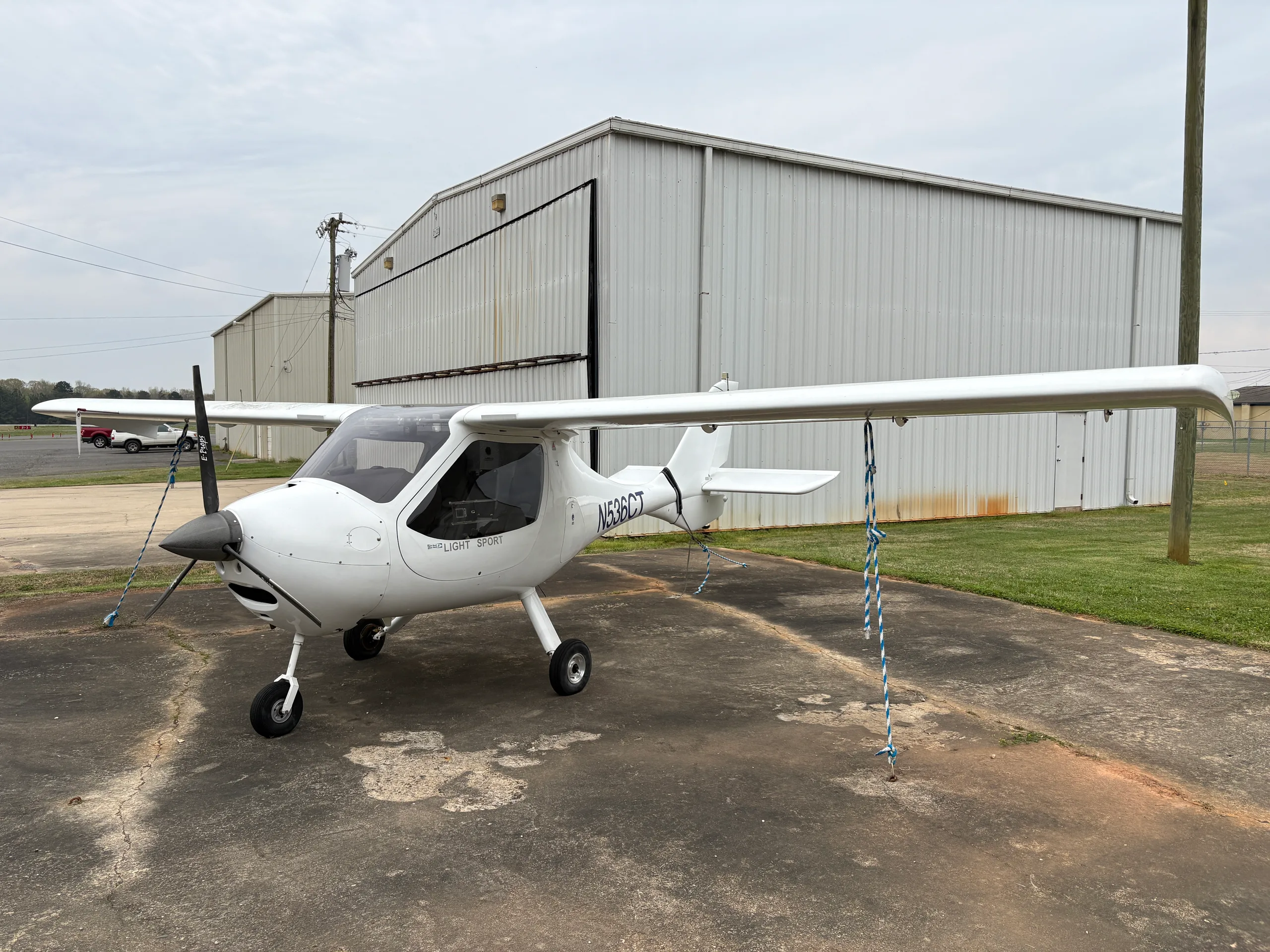 A white light sport aircraft, N536CT, is parked on a tarmac in front of a white hangar.