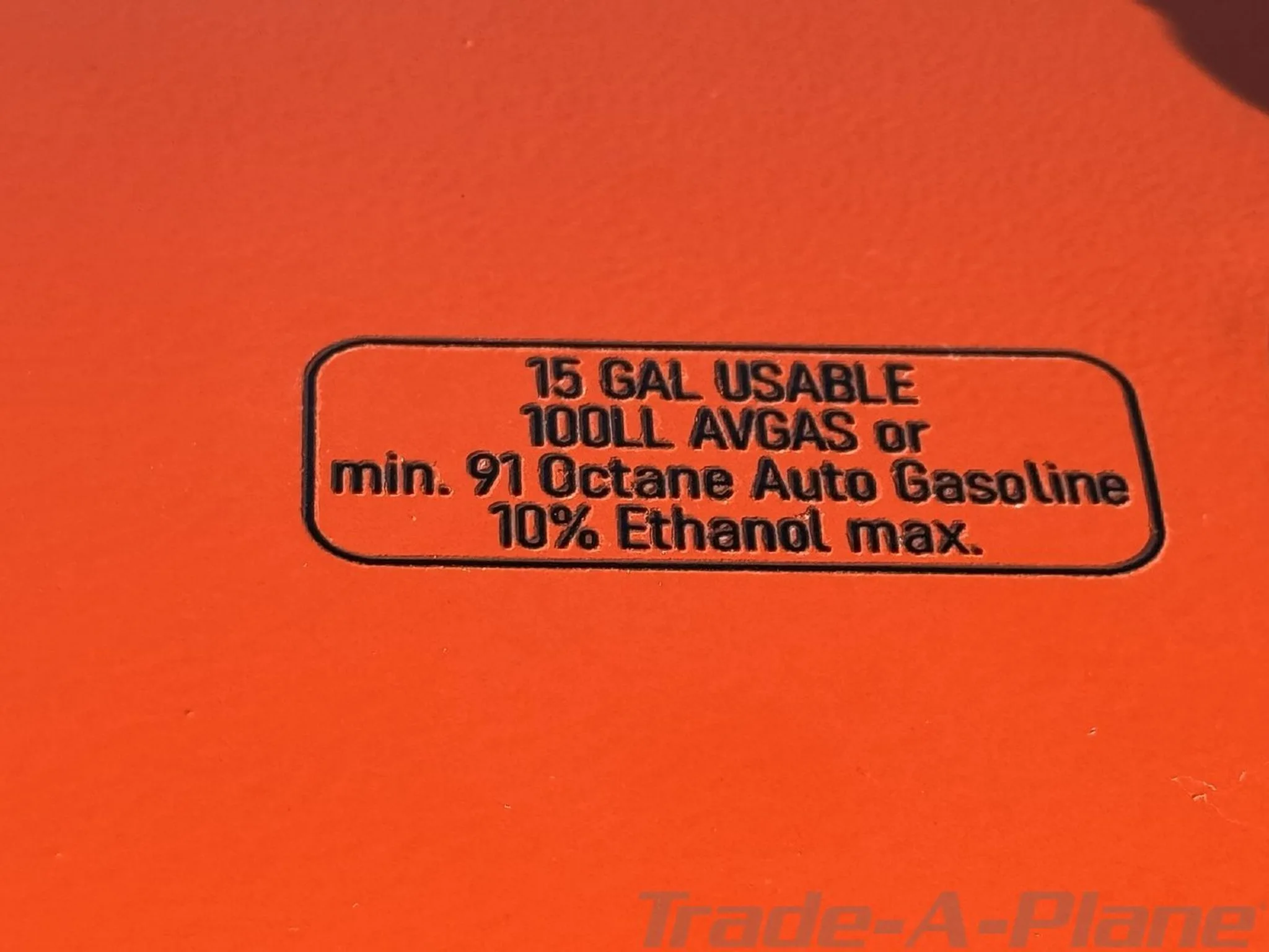 Close-up of a fuel specification label on an orange aircraft surface, indicating 15 gallons usable.