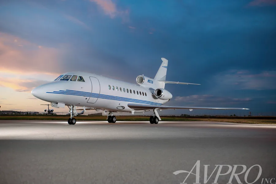 A Dassault Falcon 900EX, tail number N917JF, parked on a tarmac at sunset with blue and orange skies.