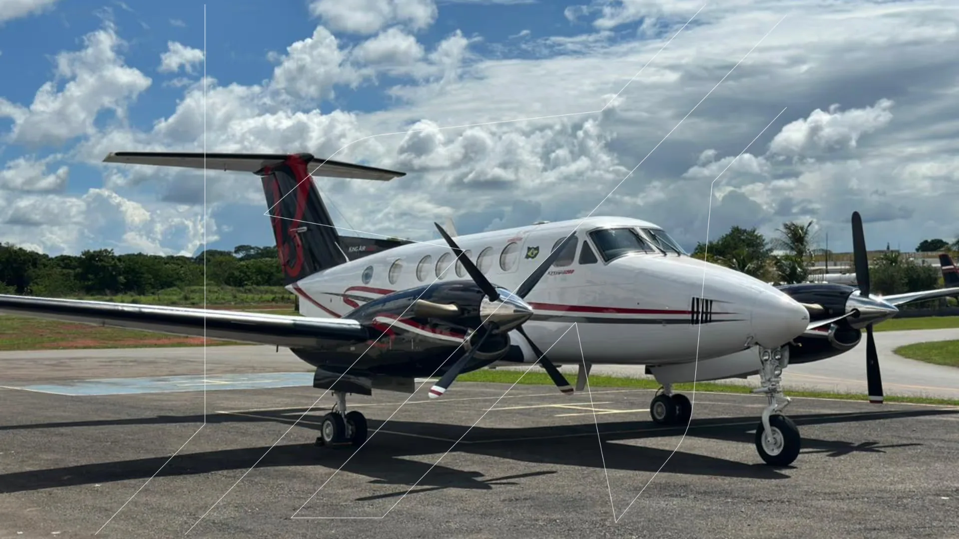 A white and black turboprop aircraft with red accents parked on an airfield under a partly cloudy sky.