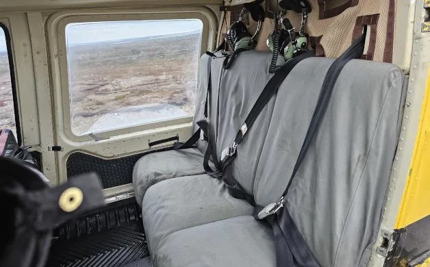 The rear cabin of a helicopter with two gray passenger seats and a view of a barren landscape through the window.