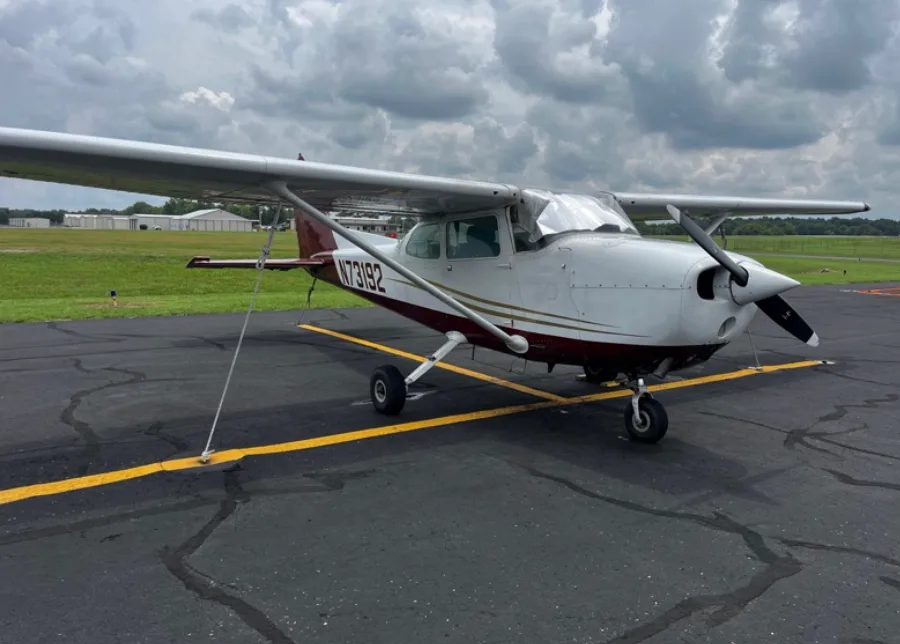 A white and maroon Cessna 172 aircraft with registration N73192 parked on an asphalt ramp under a cloudy sky.