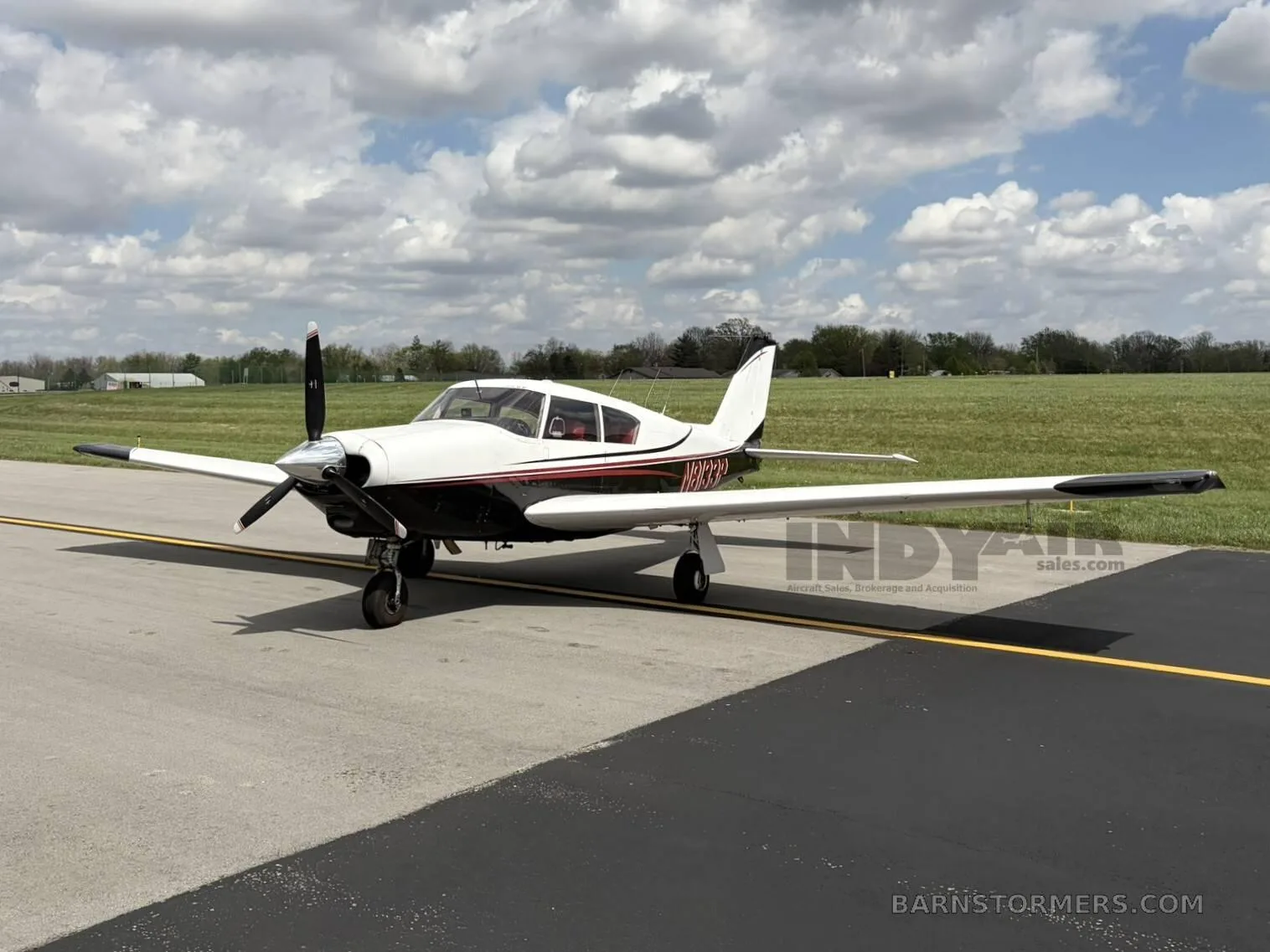 A white and black single-engine propeller aircraft with red accents, viewed from the front-right, parked on an asphalt taxiway under a cloudy sky.