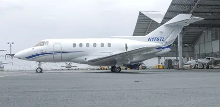 A white business jet with blue stripes, registration N176TL, parked on an apron next to a hangar.