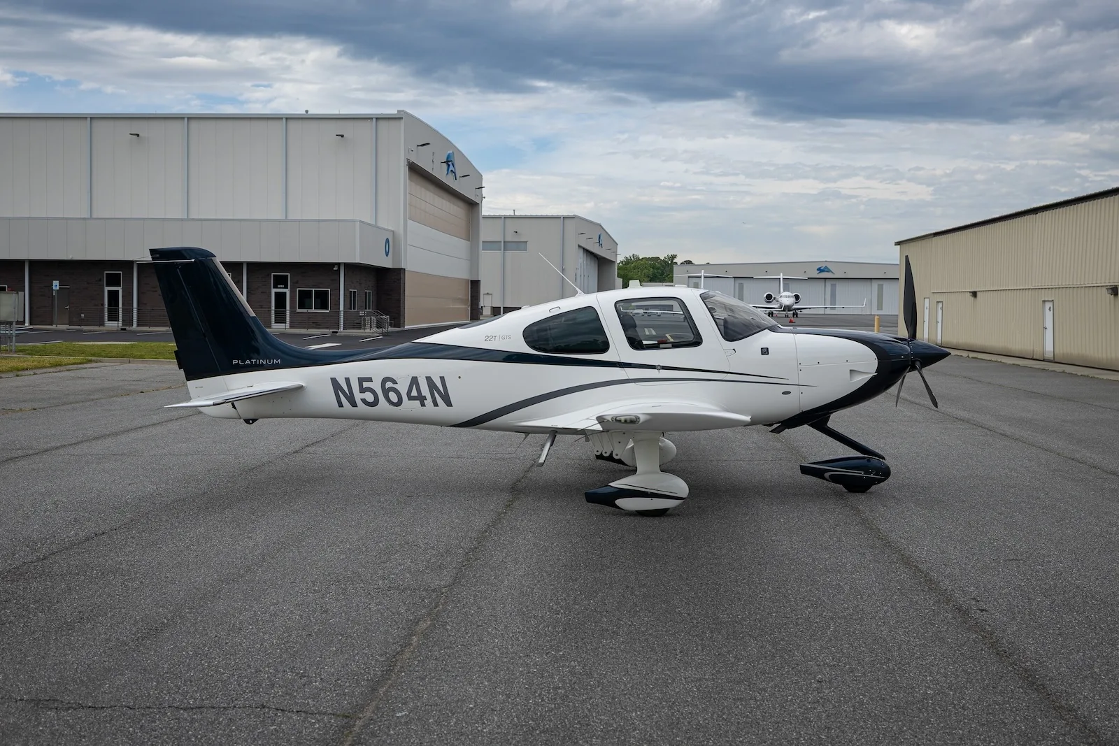A white and dark blue Cirrus SR22T aircraft with registration N564N parked on an asphalt ramp in front of hangars.