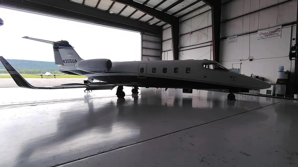A white and dark blue private jet, N355UA, parked with its tail inside a hangar and nose facing out.