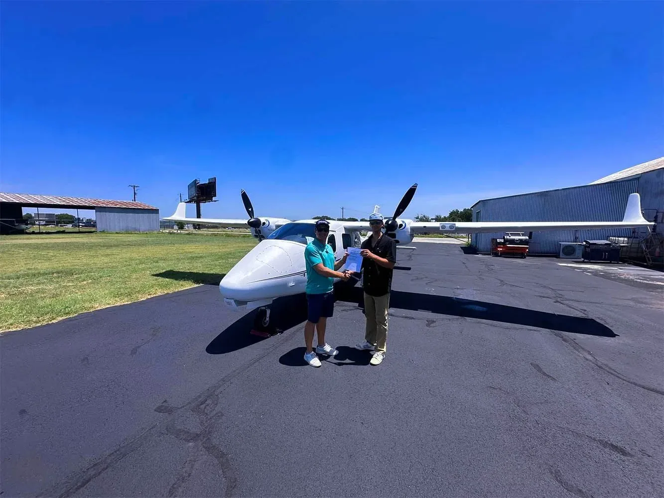 Two men shaking hands in front of a white twin-engine aircraft on an airfield on a sunny day.