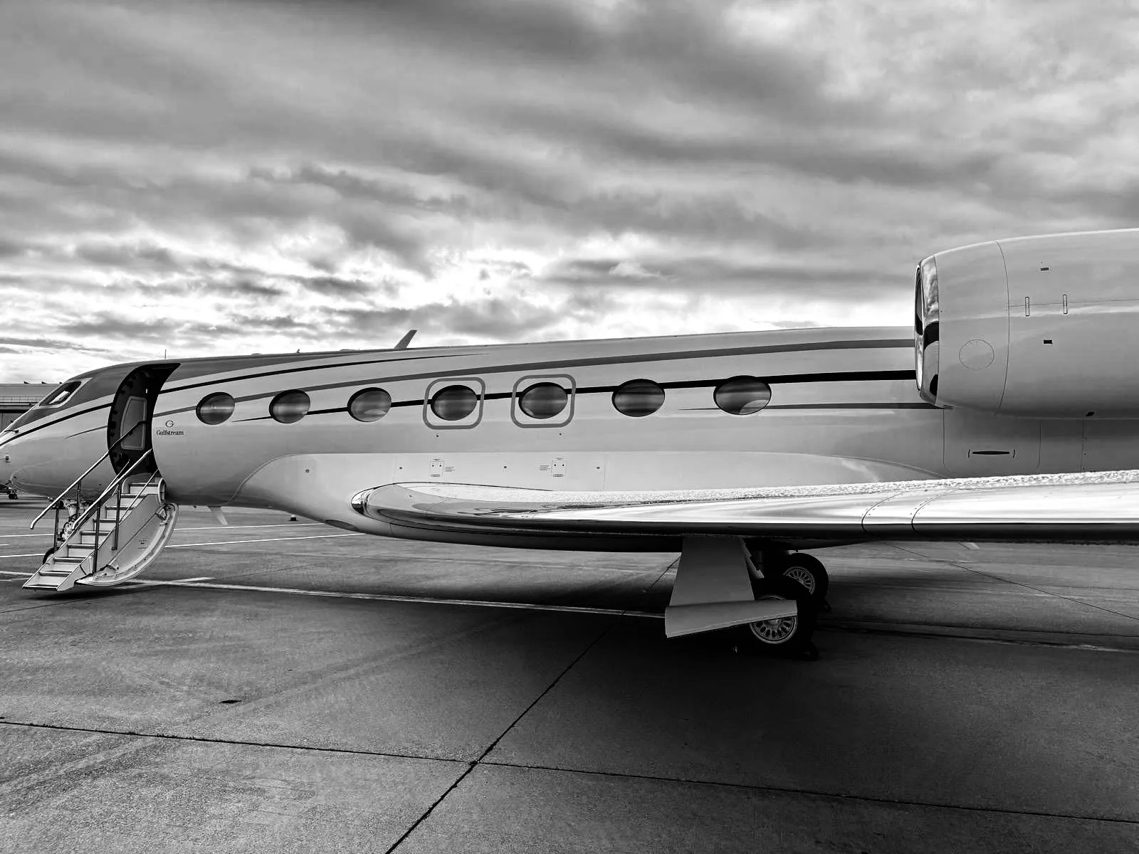 A black and white side view of a Gulfstream G650 private jet on the tarmac with its door open and stairs extended.