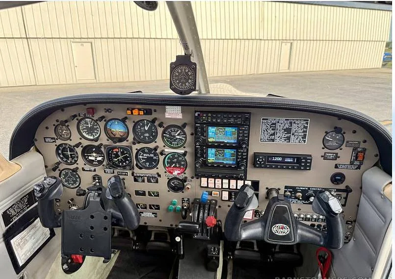 The cockpit of a Piper Arrow aircraft, showing the instrument panel with analog gauges, two Garmin GNS 430 units, and control yokes.