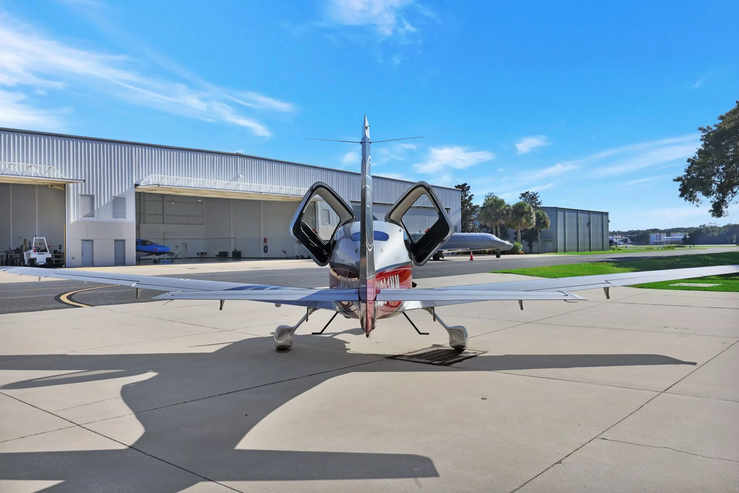 Rear view of a Cirrus SR22T aircraft with red and silver paint scheme, registration N831MM, parked on an airfield with doors open.