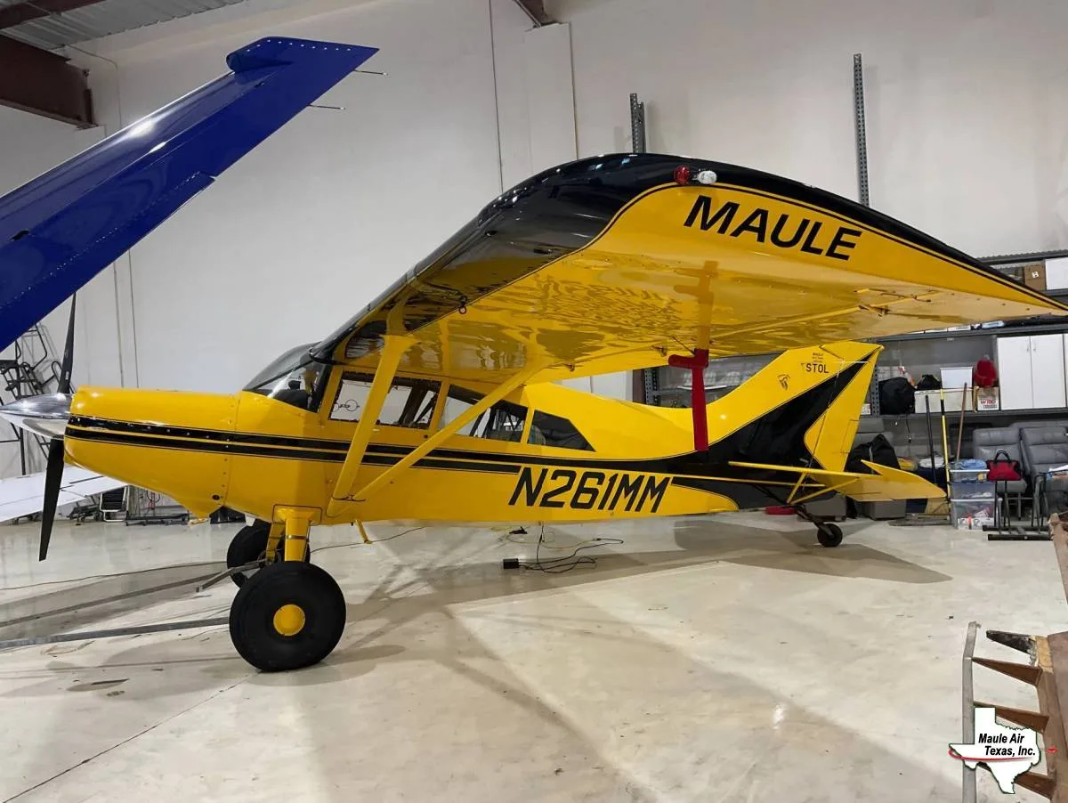 A yellow and black Maule aircraft, registration N261MM, is parked inside a hangar, viewed from the side.