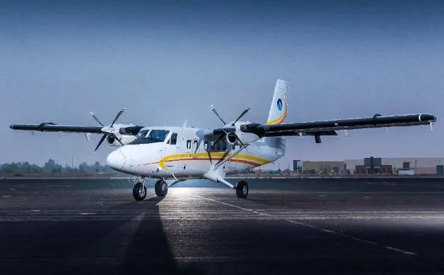 A white twin-engine turboprop aircraft with yellow and orange stripes on its fuselage, parked on an asphalt runway under a clear sky.