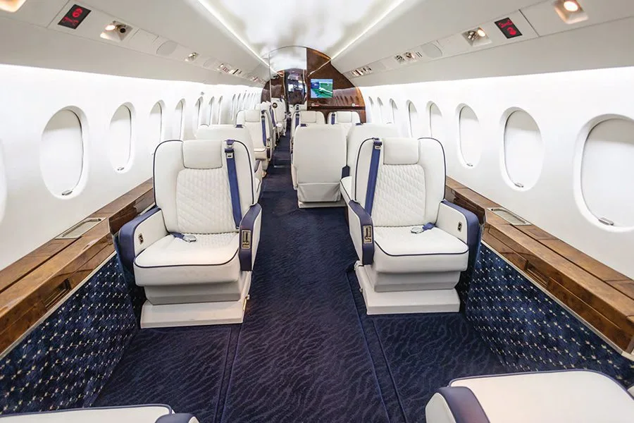 The luxurious cabin interior of a business jet with white and blue quilted seats and dark blue carpet.
