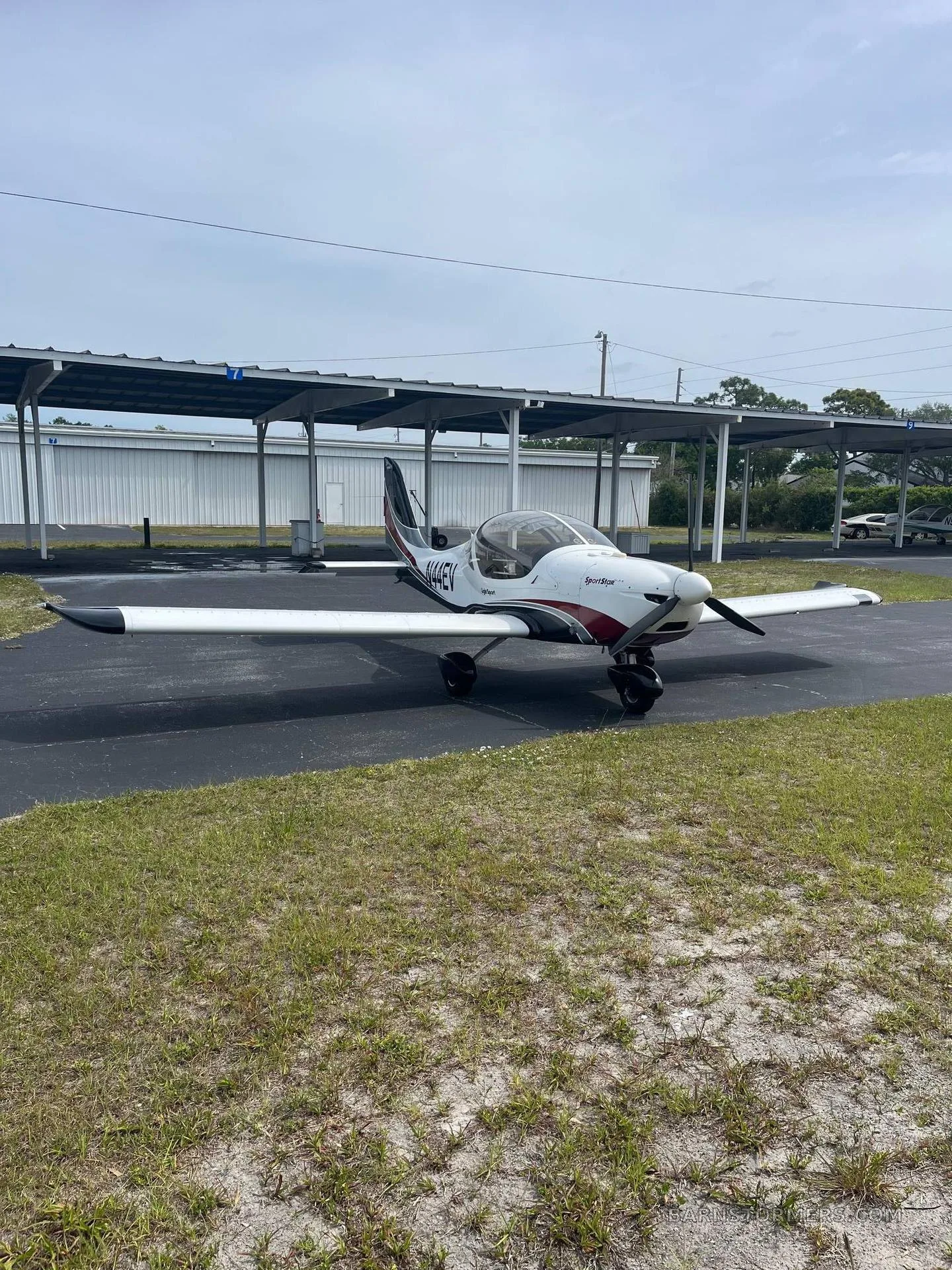 A white and red SportStar aircraft, tail number N44EV, parked on asphalt in front of an open hangar.