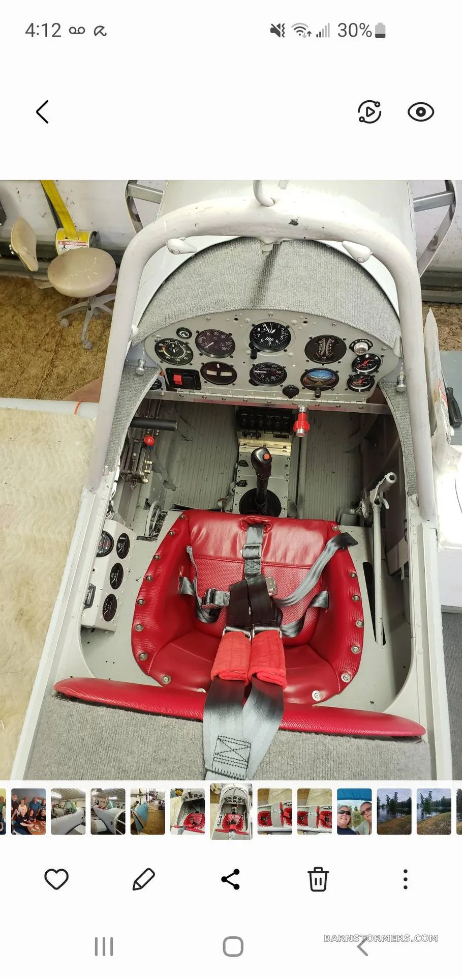 The cockpit of a light grey aircraft, showing the instrument panel and a red seat with a harness.