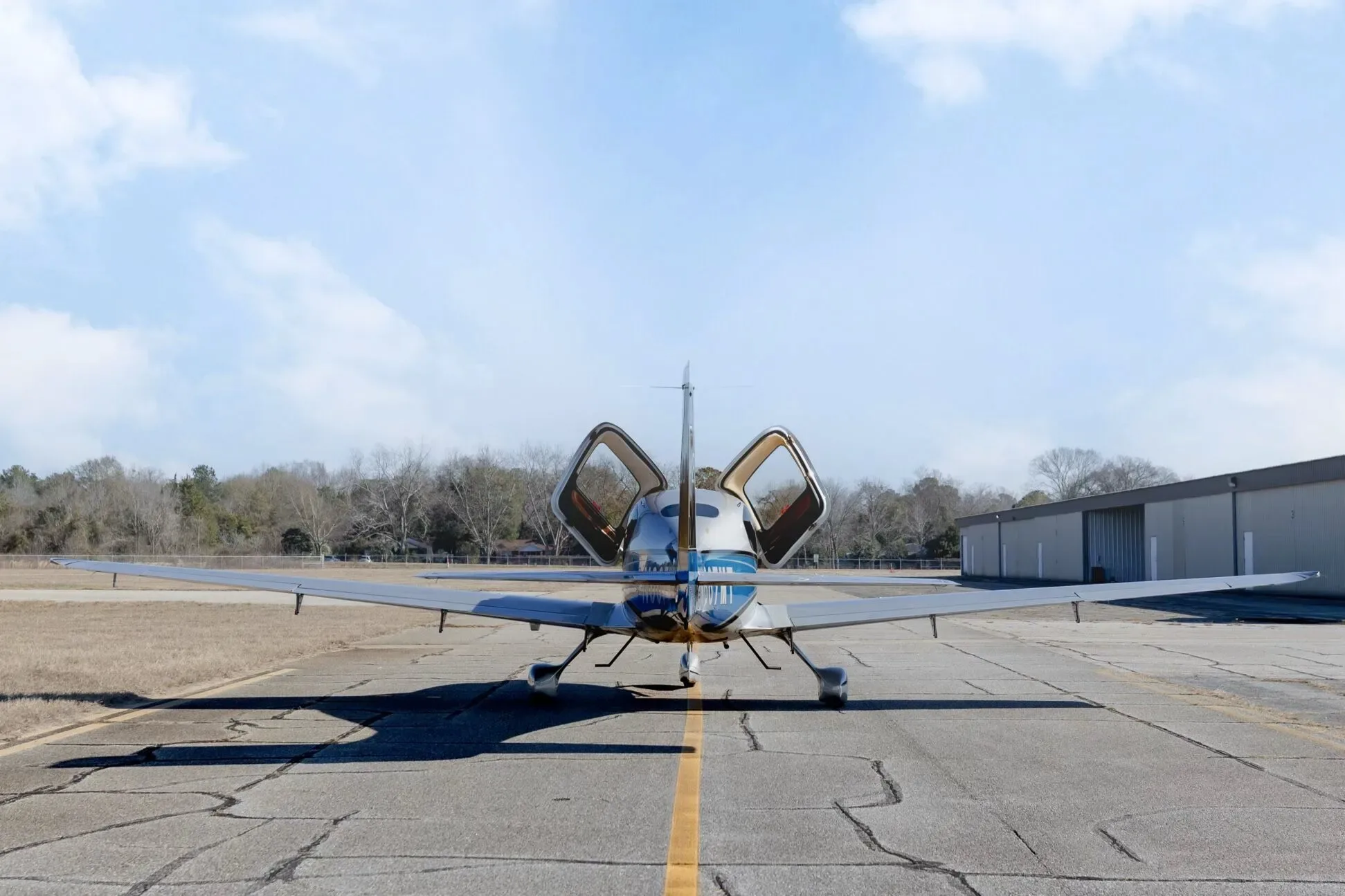 A rear view of the Cirrus SR20 GTS aircraft with N667MT registration, showing its open gull-wing doors on an airfield.