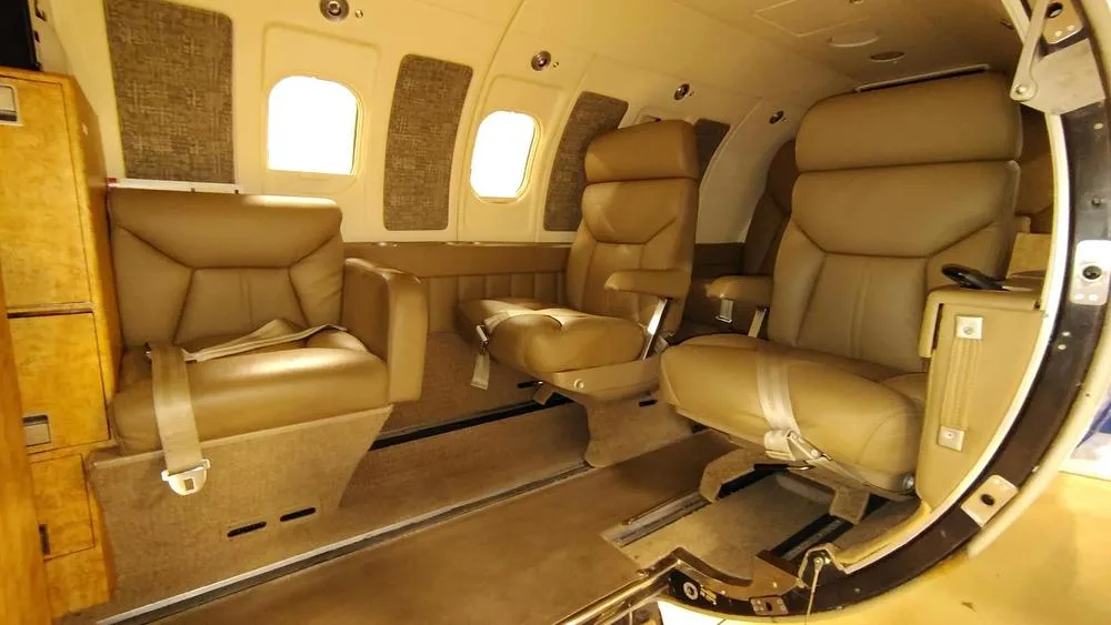 The tan leather interior cabin of a private jet, showing multiple seats and windows from the entry.