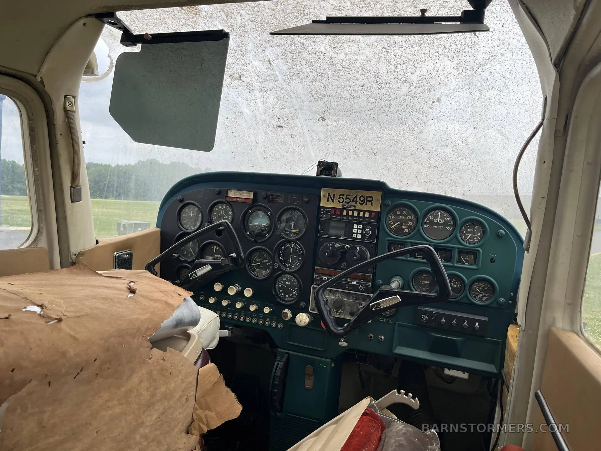 The cockpit of a single-engine aircraft, registration N5549R, showing a green instrument panel with various gauges and controls, and a dirty windshield.