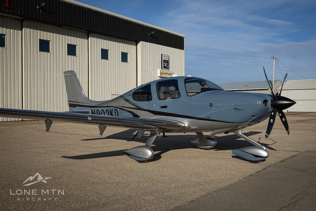 A Cirrus SR22T aircraft, N902KD, in blue and silver paint, parked on an airfield in front of a hangar.