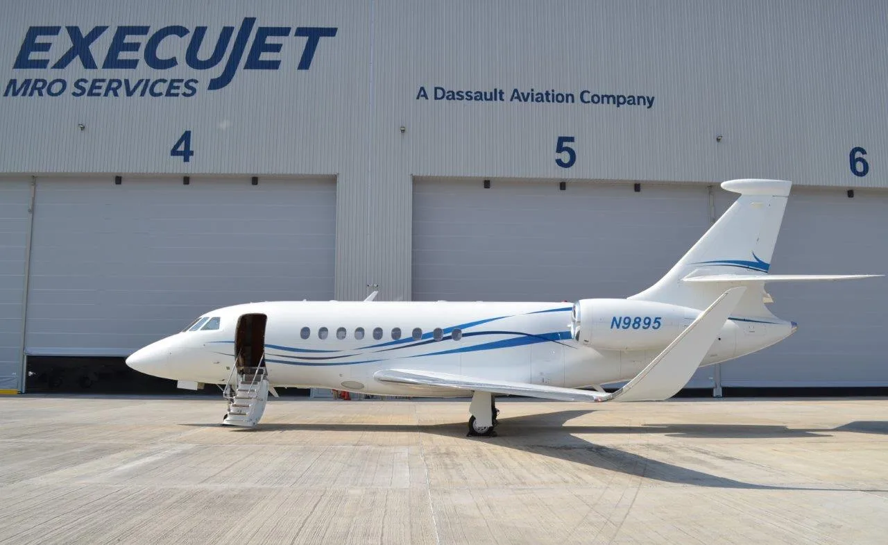 A white business jet with blue swooping lines is parked on a tarmac in front of an ExecuJet MRO Services hangar.