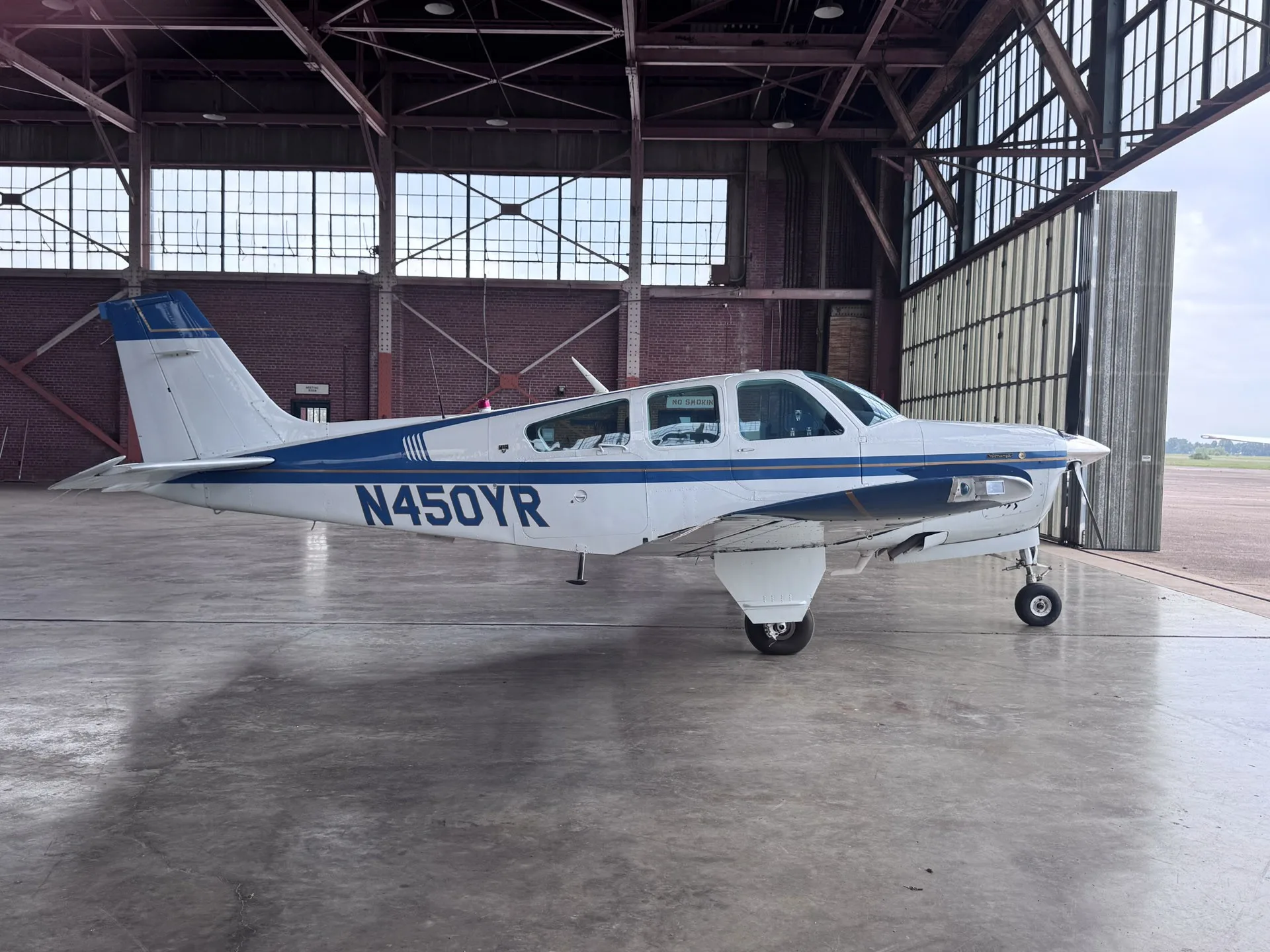 A white and blue Beechcraft Bonanza F33A aircraft with registration N450YR parked in a hangar.