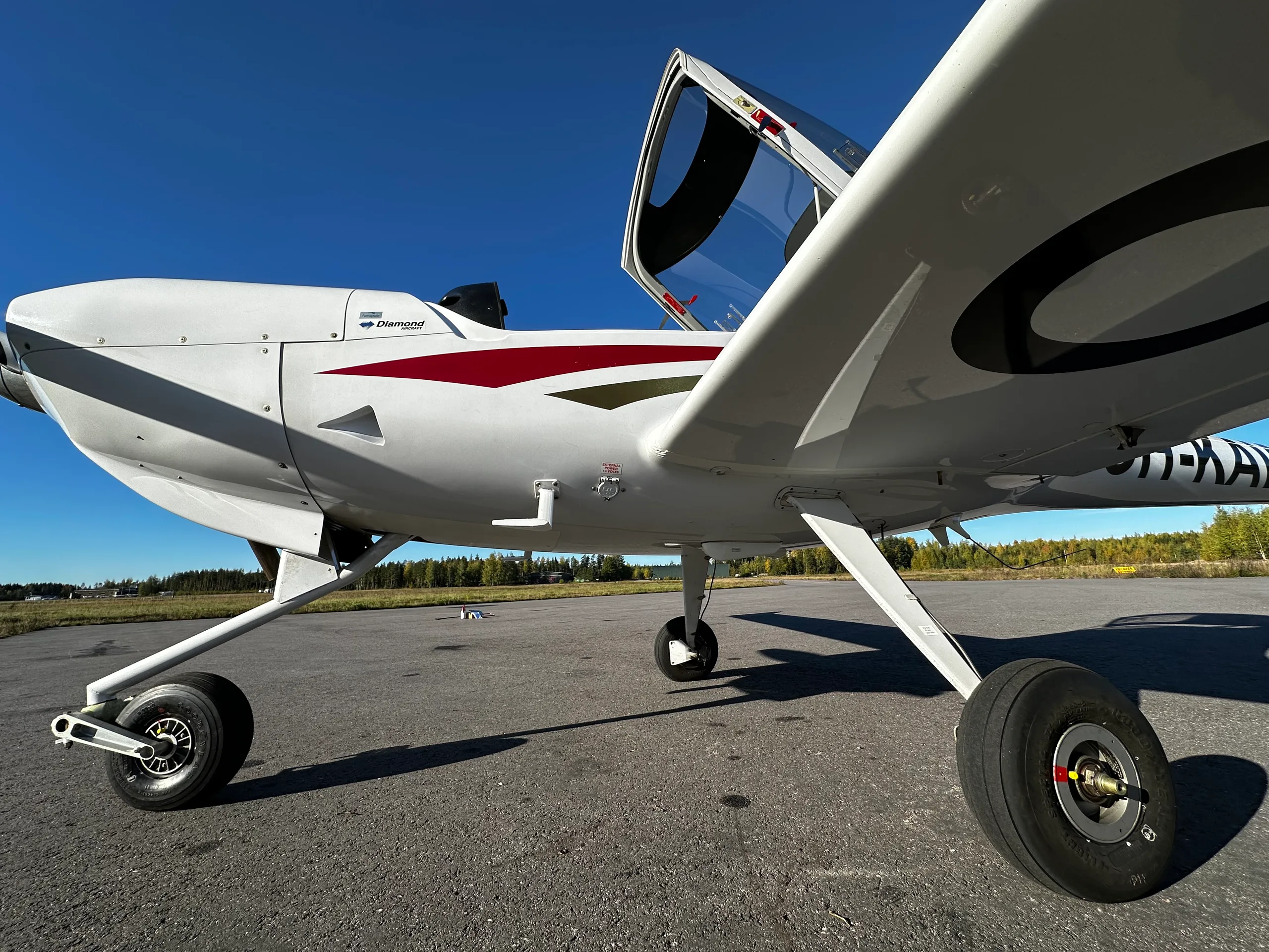 A close-up view of the white Diamond DA20 fuselage and main landing gear, showing the 'Diamond' logo and red/black stripes.